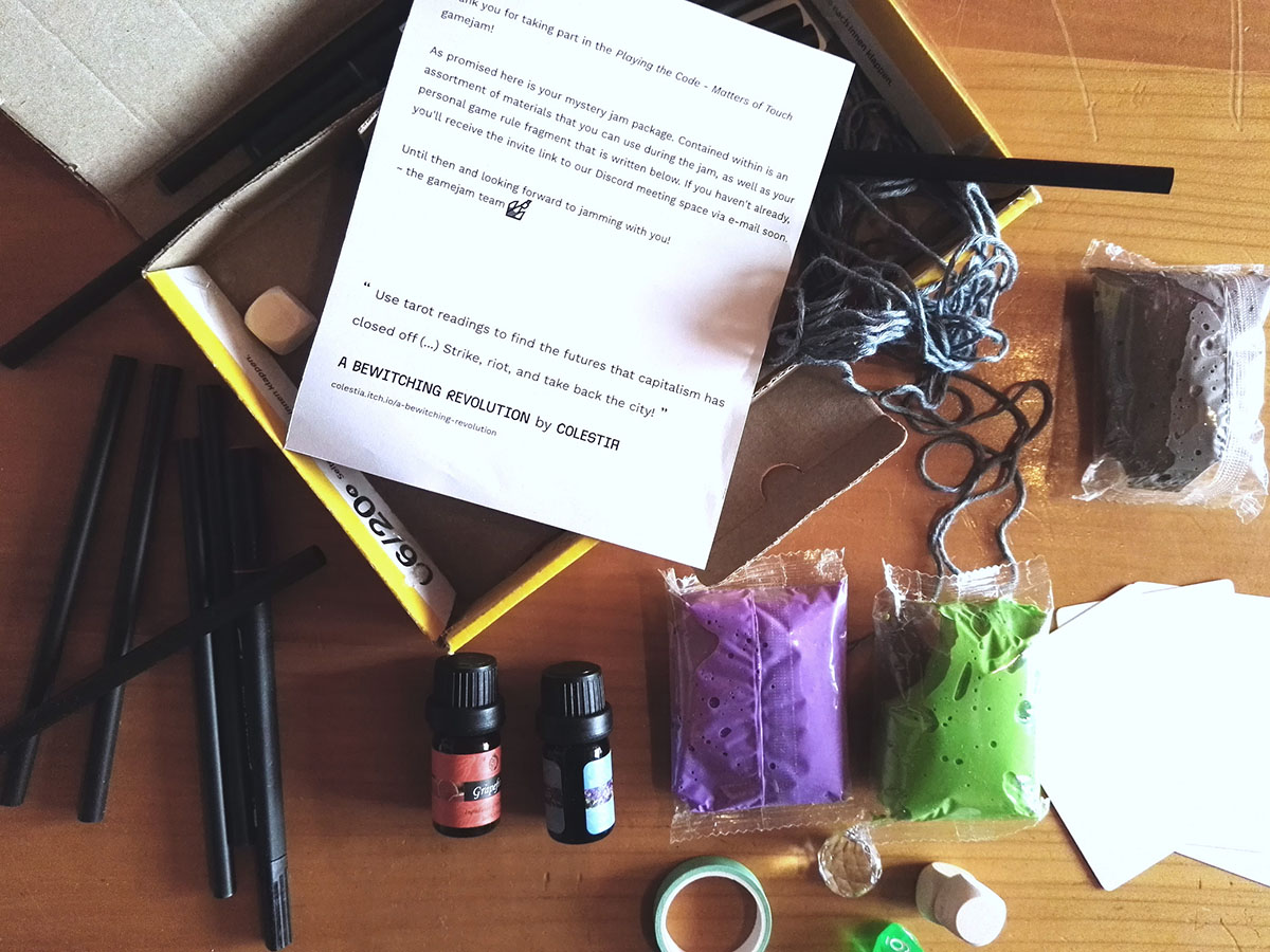 A small opened parcel. Various crafting materials are spilling out of it: yarn, pens, tape, dice, playing cards, modelling clay as well as a small printed note from the gamejam organizers. On the bottom of the note is a quote: "Use tarot readings to find the futures that capitalism has closed of (...) Strike, riot and take back the city!" - A Bewitching Revolution by Colestia.